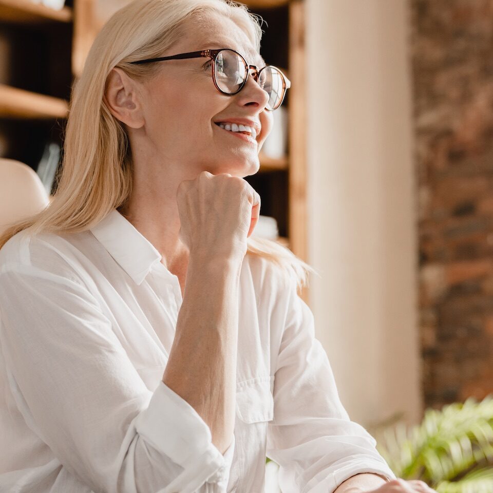 Happy pensive caucasian middle-aged mature businesswoman ceo freelancer teacher boss dreaming thinking about new startup ideas, planning future project while working in office